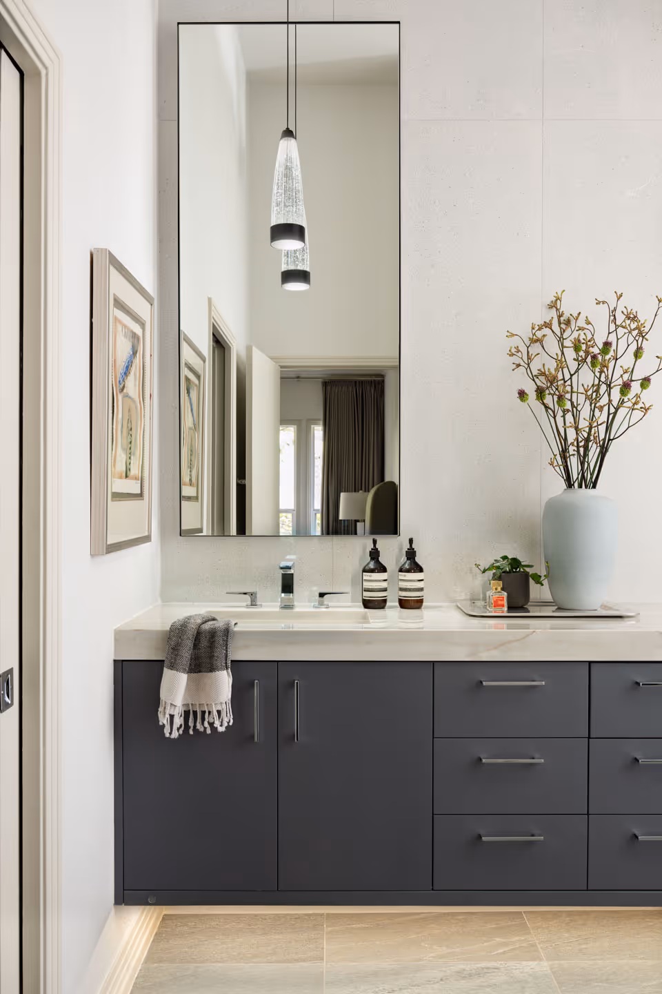Bright modern bathroom with freestanding white bathtub beneath large windows, double wooden vanities with marble countertops and large mirrors.