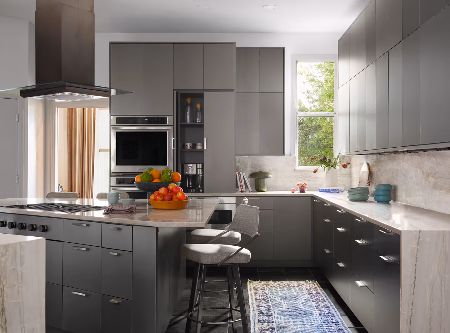 Modern open living space with wooden floors, a wall-mounted TV above a sleek fireplace, and a kitchen island with bar stools and pendant lights.