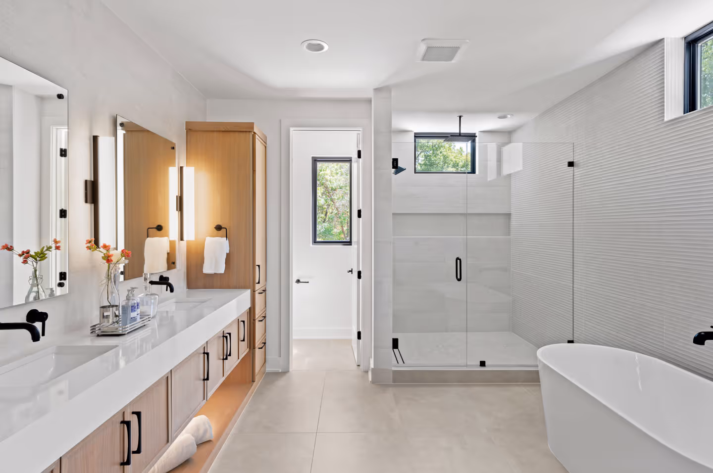 Modern bathroom with dual sinks, wooden cabinetry, walk-in glass shower, and a freestanding white bathtub.