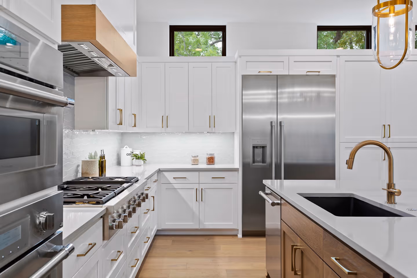 Modern kitchen with white cabinetry, stainless steel appliances, wooden floor, and a kitchen island with a gold faucet.
