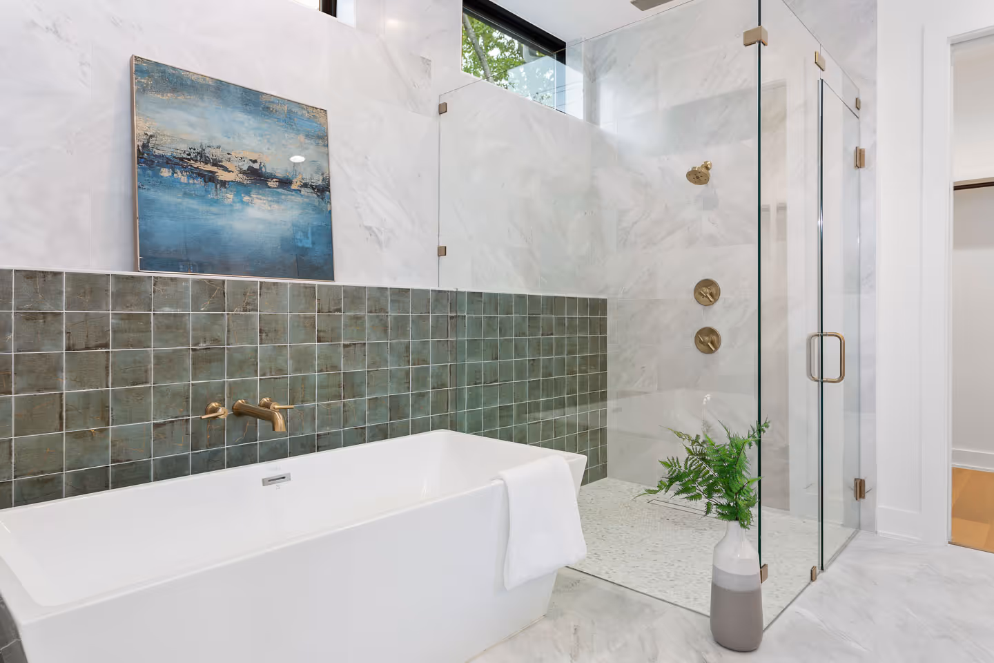 Modern bathroom with a white freestanding bathtub, green tiled wall, glass shower enclosure, and a painting above the tub.