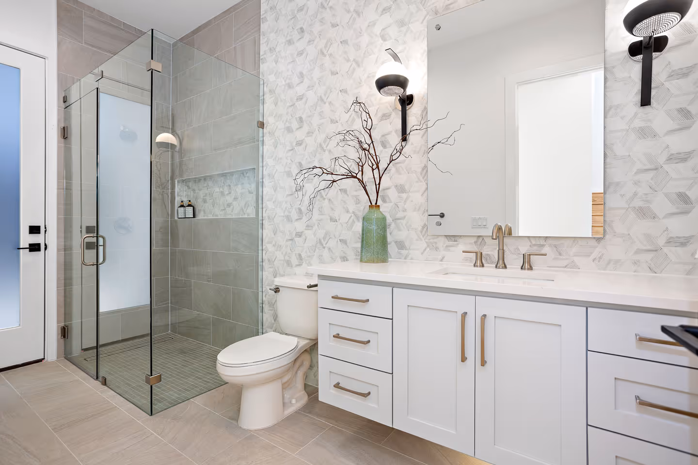 Modern bathroom with glass shower enclosure, white toilet, floating vanity with white cabinetry, and decorative vase with branches on the countertop.