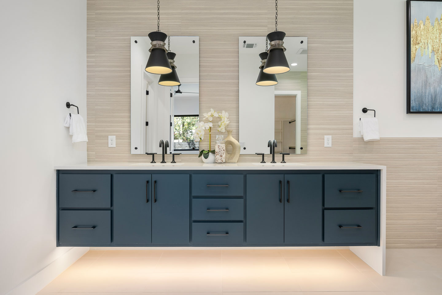 Modern bathroom vanity with dark blue cabinets, two black pendant lights, double mirrors, and a white orchid centerpiece on the countertop.