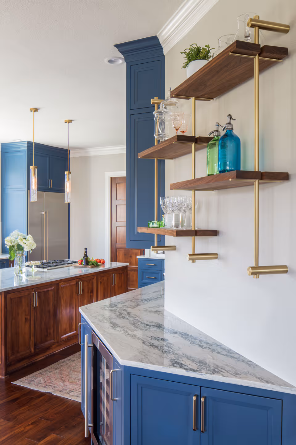 Modern kitchen with blue cabinets, marble countertops, wooden island with cooktop, and hanging pendant lights.