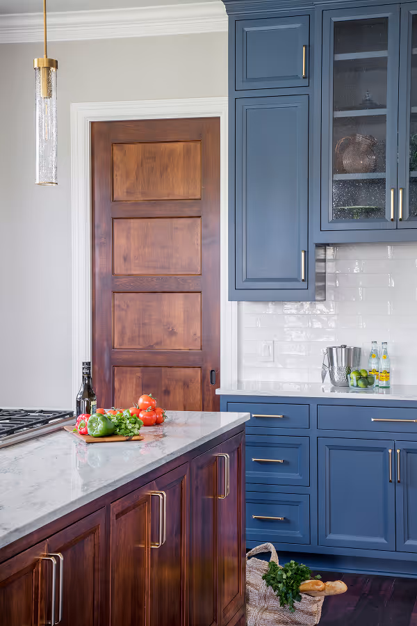 Modern kitchen with blue cabinets, marble countertops, wooden island with cooktop, and hanging pendant lights.