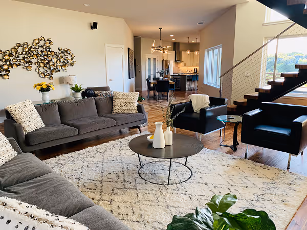 Modern open living space with wooden floors, a wall-mounted TV above a sleek fireplace, and a kitchen island with bar stools and pendant lights.