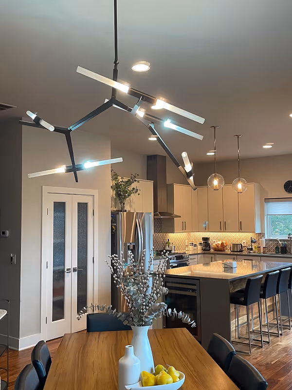 Modern open living space with wooden floors, a wall-mounted TV above a sleek fireplace, and a kitchen island with bar stools and pendant lights.