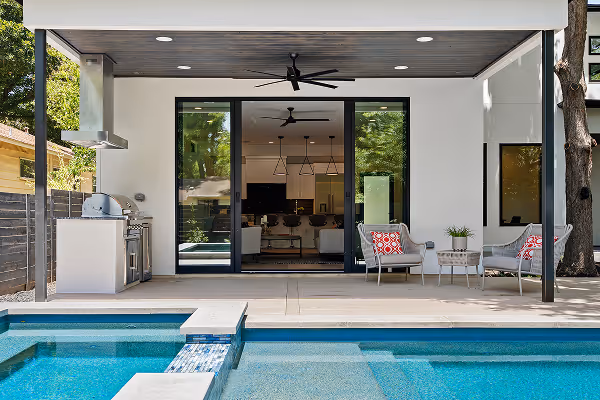Modern backyard patio with stainless steel grill, seating area, and a clear blue swimming pool.